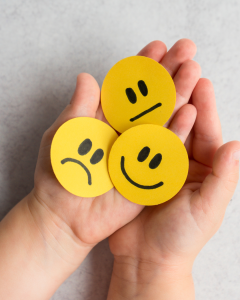 Two hands cradling three yellow faces - one smiling, one neutral and one sad